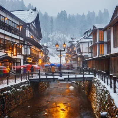 Hiver au Japon – Entre paysages enneigés, onsen et traditions Village japonais enneigé avec rivière et lumières en hiver Japon